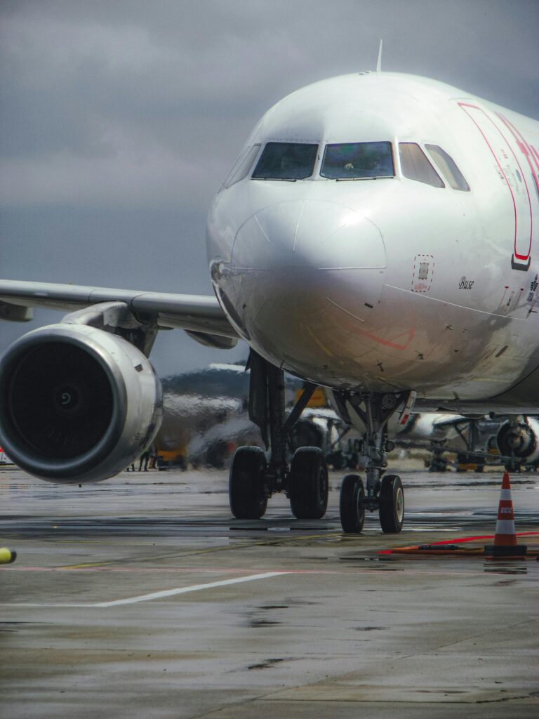 A large commercial airplane taxiing on a wet runway at an airport under cloudy skies.